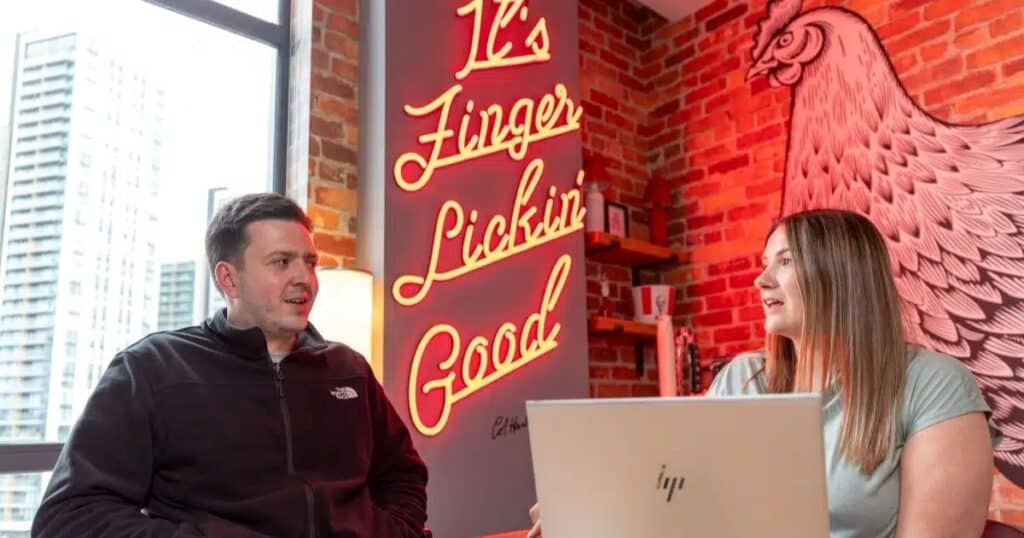 Two people talk while at work in the KFC UK headquarters in Woking. One of them has a laptop in front of them.
