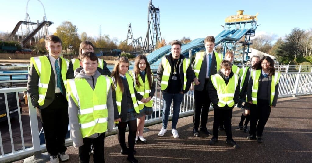 Young people and adults wearing high vis jackets pose in front of a theme park attraction.